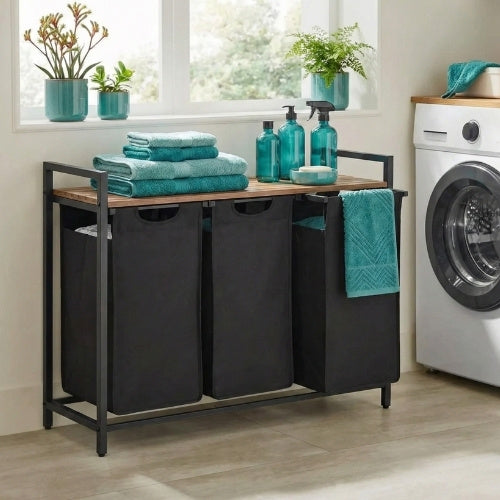 Gemini said Rivercity Furniture black 3-bag laundry sorter in a modern Australian home. Styled with signature teal towels, bottles, and plant pots on its slatted top, placed next to a washing machine.
